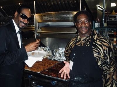 Reo Varnado is on his apron as Snoop Dogg is eating his food.